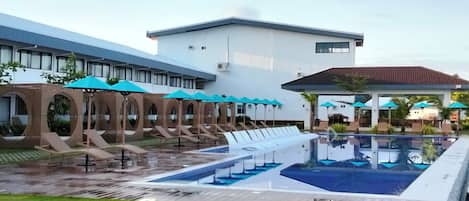 A hotel with a swimming pool, lounge chairs, and umbrellas.