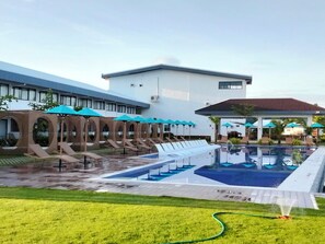 A hotel with a swimming pool, lounge chairs, and umbrellas. - Hudor Resort (Bauang)