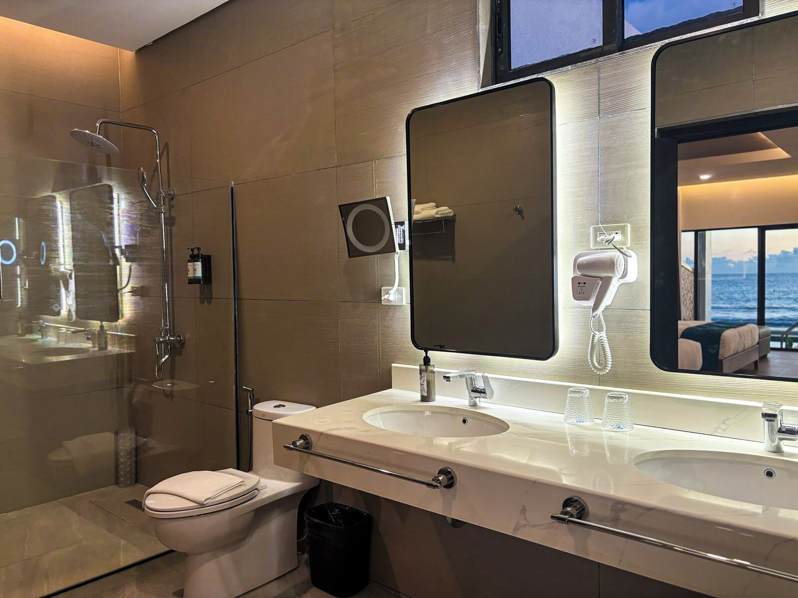 Une salle de bain moderne dotée d’un double lavabo, d’un grand miroir, d’une douchette à main et de toilettes.