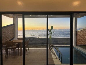 A balcony with a view of the ocean at sunset, a pool, and wicker furniture. - Hudor Resort (Bauang)