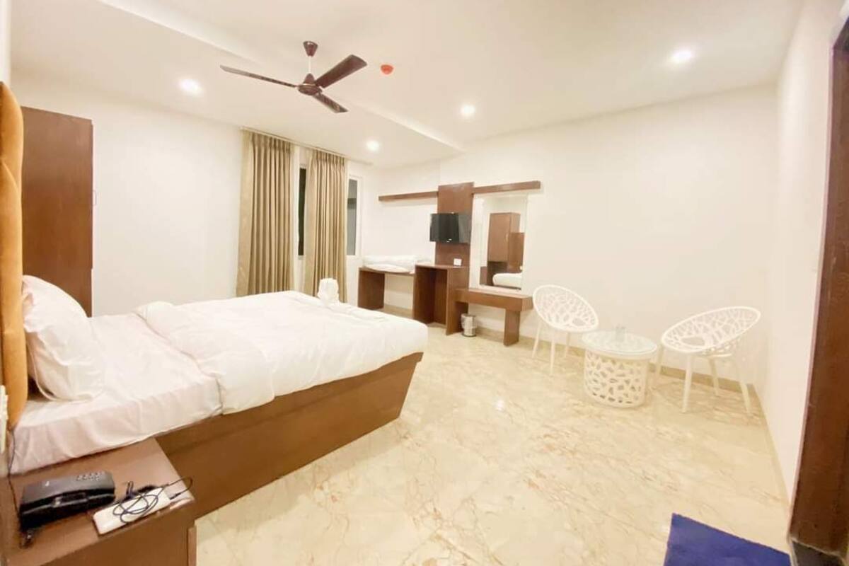 A modern hotel room with a large bed, a desk, a chair, a small table, and a ceiling fan.