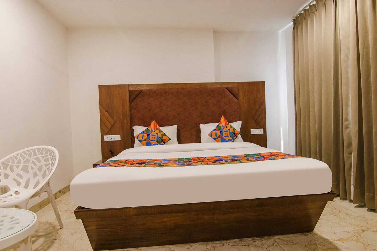 A neatly made bed with a wooden headboard, two pillows with geometric patterns, and a white bedside table.