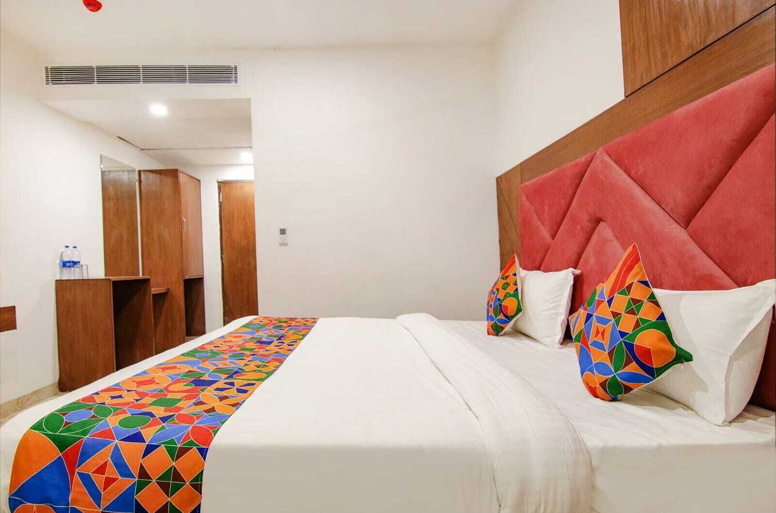 Una habitación de hotel con una cama, cabecero, colcha colorida y armario de madera.