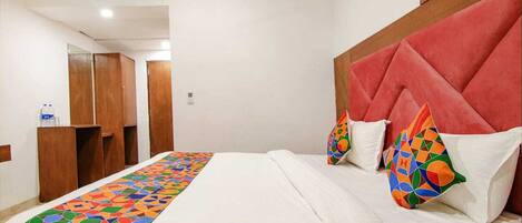 Una habitación de hotel con una cama, cabecero, colcha colorida y armario de madera.
