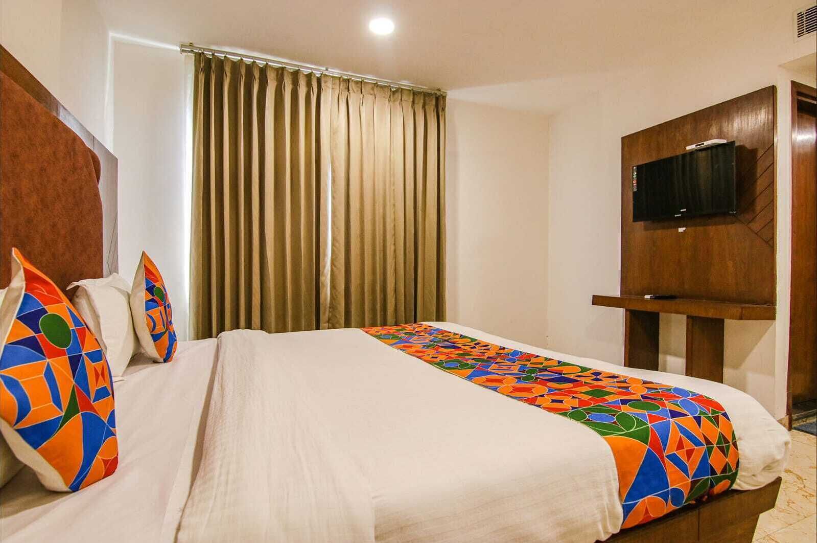 A hotel room with a bed, a TV mounted on the wall, and a window with curtains.