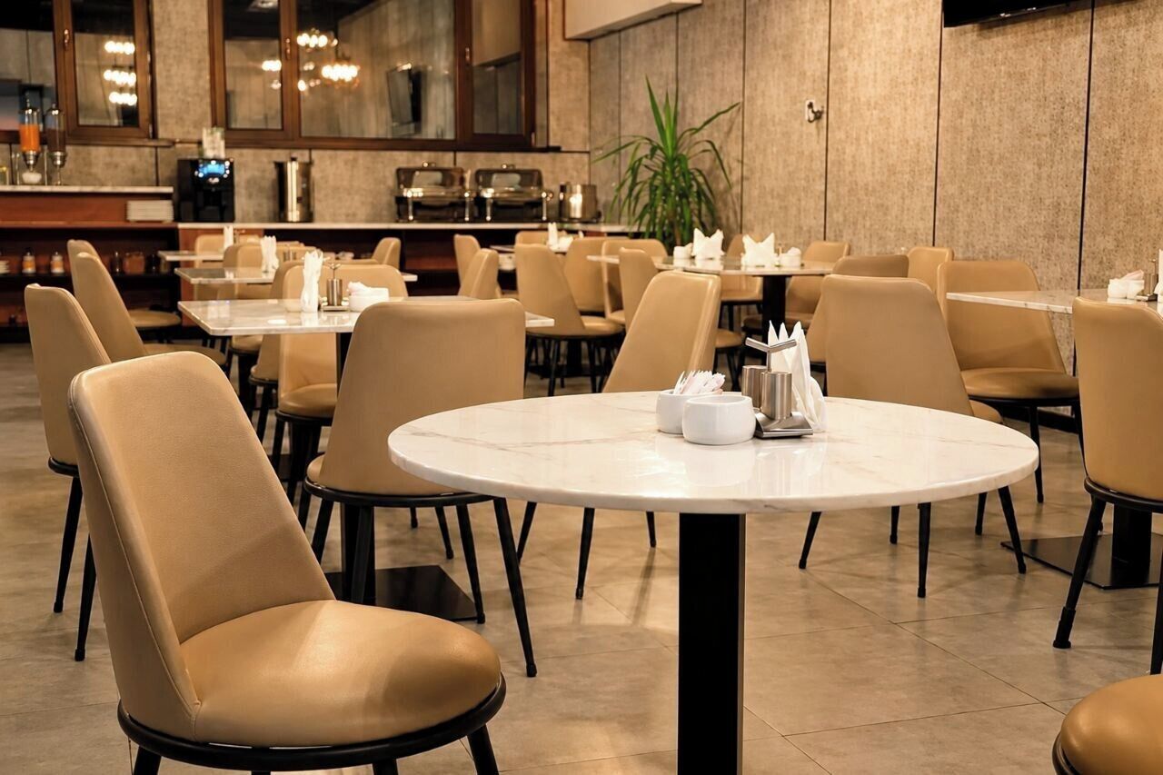 A restaurant with round tables and chairs, a bar area, and a potted plant.