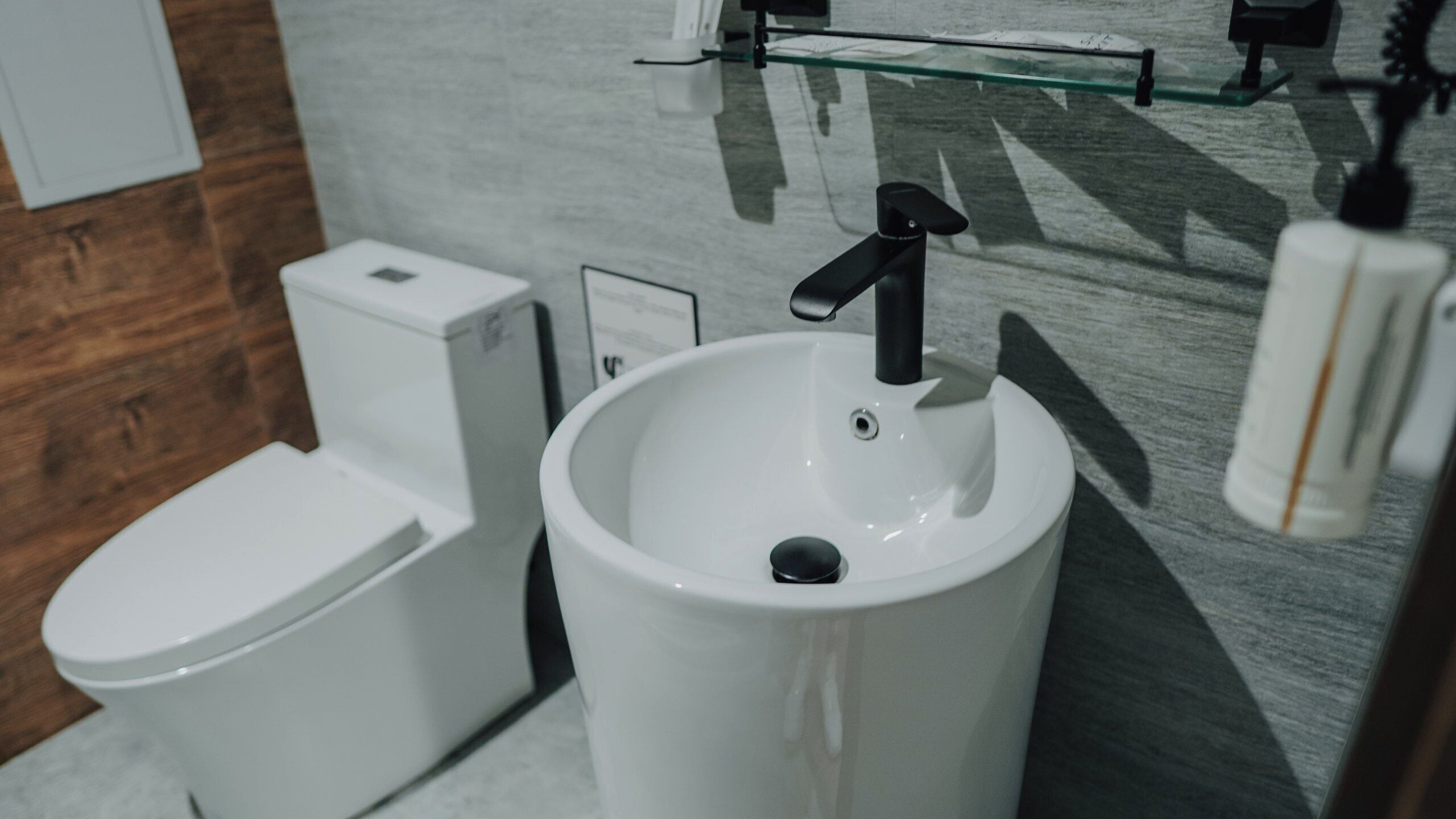 A modern bathroom with a toilet, sink, and a glass shelf above the sink.