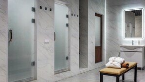 A modern bathroom with marble walls, a bench with towels, and a mirror above the sink.