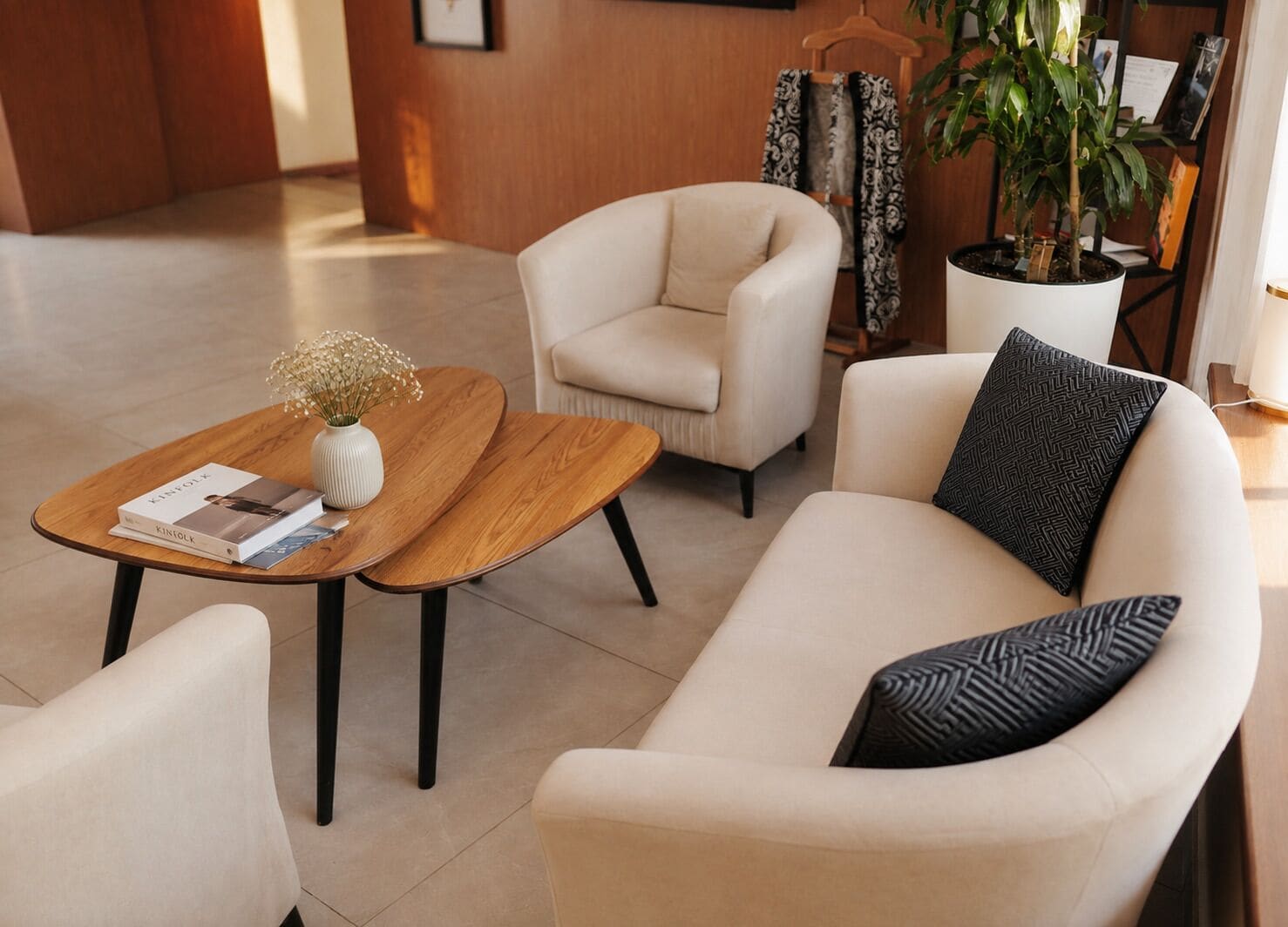 A modern lounge area with a sofa, armchairs, a wooden coffee table, and a potted plant.