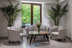 A modern living room with a round table, two armchairs, and large potted plants.