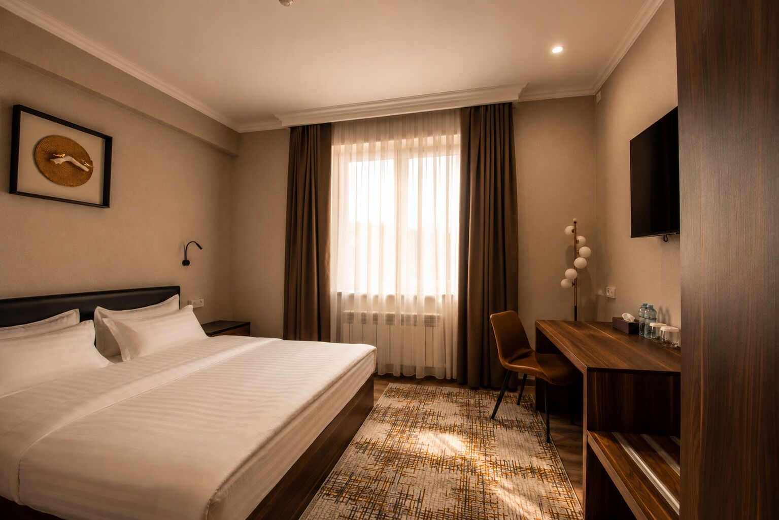 Une chambre d’hôtel avec un lit, un bureau, une chaise, une télévision et une fenêtre avec des rideaux.