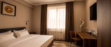 Une chambre d’hôtel avec un lit, un bureau, une chaise, une télévision et une fenêtre avec des rideaux.
