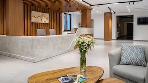 A modern reception area with a wooden reception desk, a seating area with a grey sofa, and a coffee table with magazines.