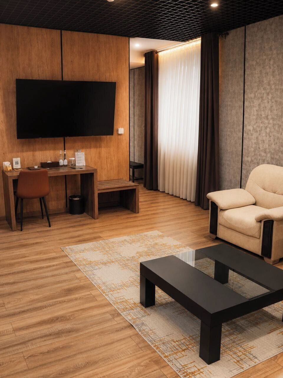 A modern living room with a flat-screen TV, a sofa, a coffee table, and a desk with a chair.