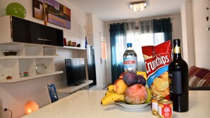 A kitchen counter with a bowl of fruit, a bottle of water, a can of beans, a bottle of wine, and a bag of crisps. - Oasis Marítimo en Güímar (Puertito de Güímar)