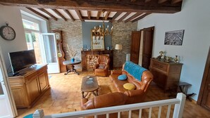 A living room with a leather sofa, wooden coffee table, and a television. There is a fireplace with a mirror above it, and a chandelier hanging from the ceiling. - Charmant Gite aux Beaux Volumes, Jardin Privé, Idéal en Familles (Beaumont-de-Lomagne)