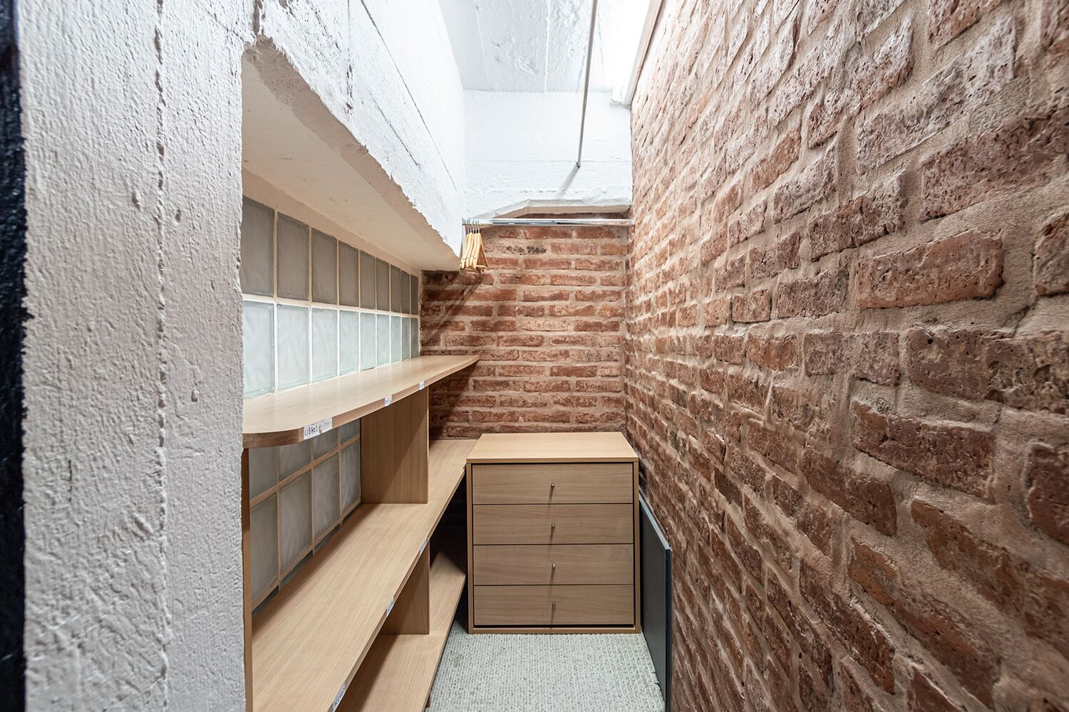 A narrow hallway with exposed brick walls, a wooden bench, and a small cabinet.