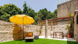 Een terras met een gele parasol, een loungestoel en een klein tafeltje.