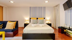 Een moderne hotelkamer met een groot bed, twee nachtkastjes, een bank en een televisie.