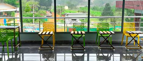 Une pièce dotée d’une grande fenêtre donnant sur un paysage verdoyant, d’un sol carrelé et de trois chaises au design original.