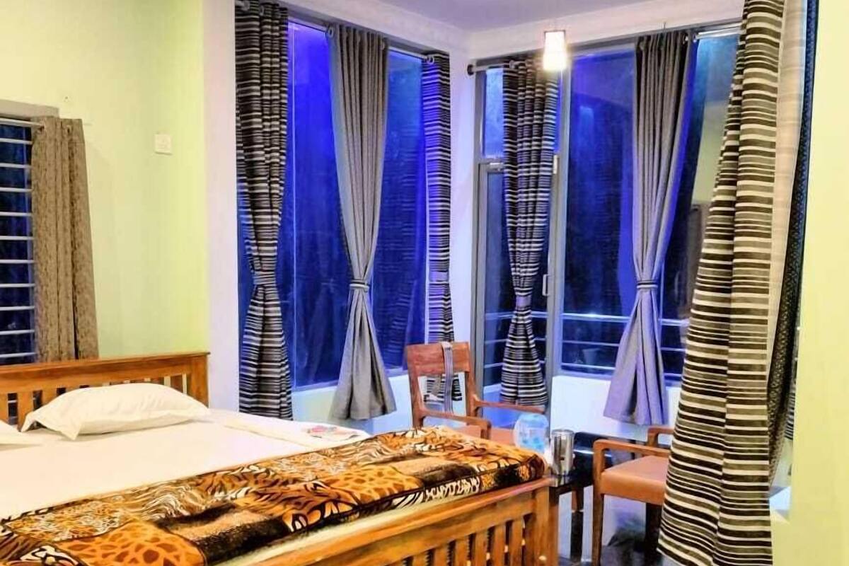 Ein Schlafzimmer mit einem Holzbett, einer gemusterten Tagesdecke und Blick durch große, mit Vorhängen versehene Fenster nach draußen.
