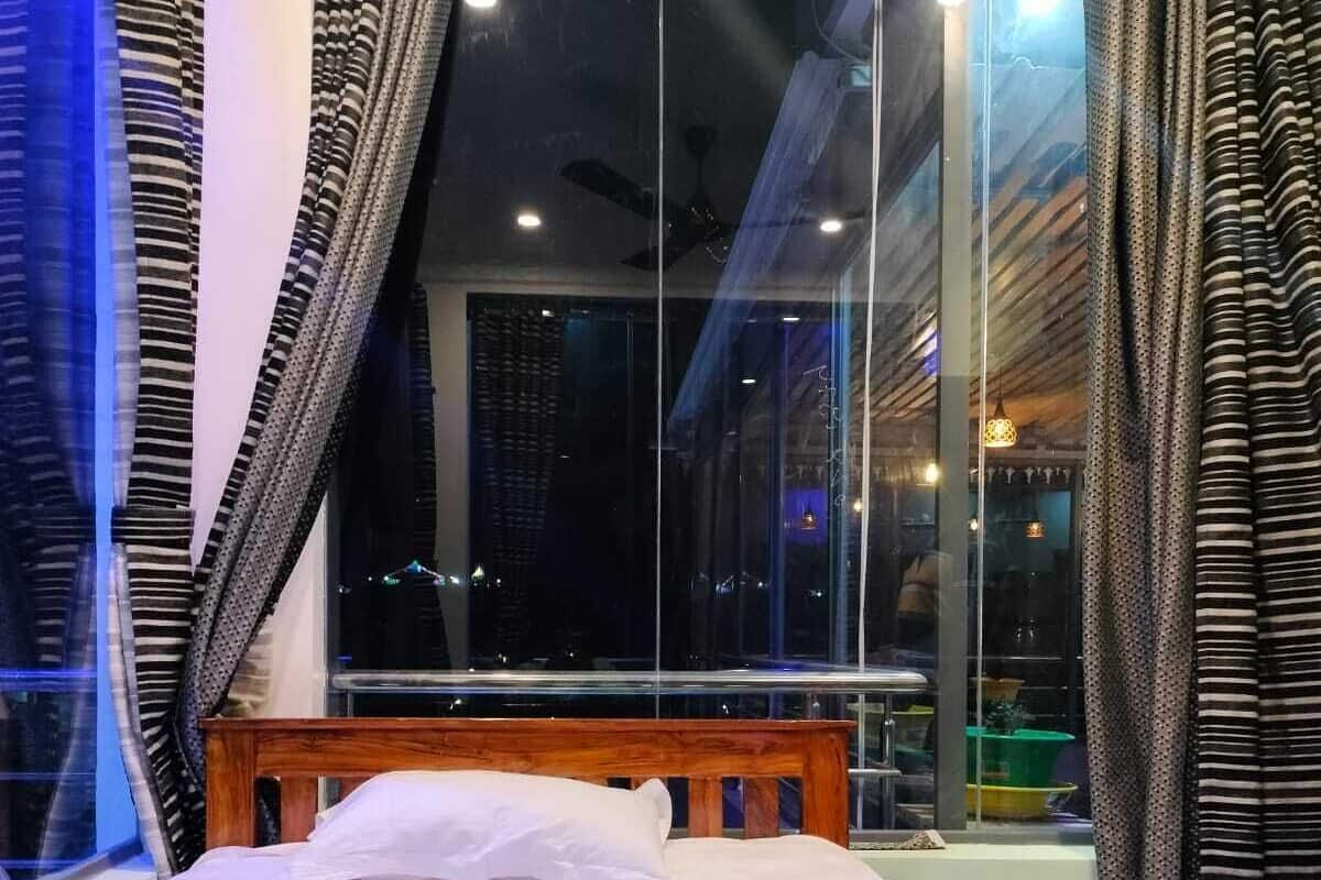 Ein Hotelzimmer mit einem großen Bett, Blick auf die beleuchtete Stadt bei Nacht und Vorhängen an den Fenstern.