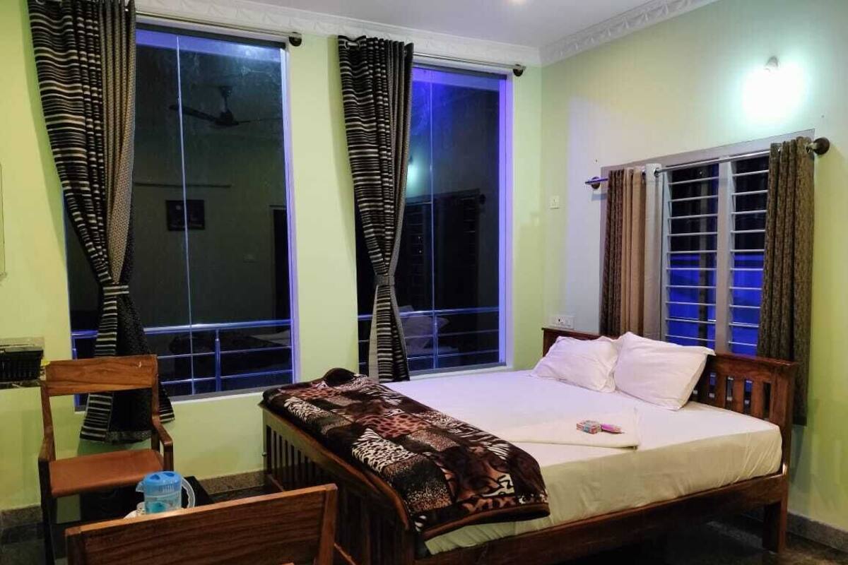 Ein Schlafzimmer mit einem hölzernen Bett, zwei mit Vorhängen versehenen Fenstern, einem Sessel und einem Nachttisch.