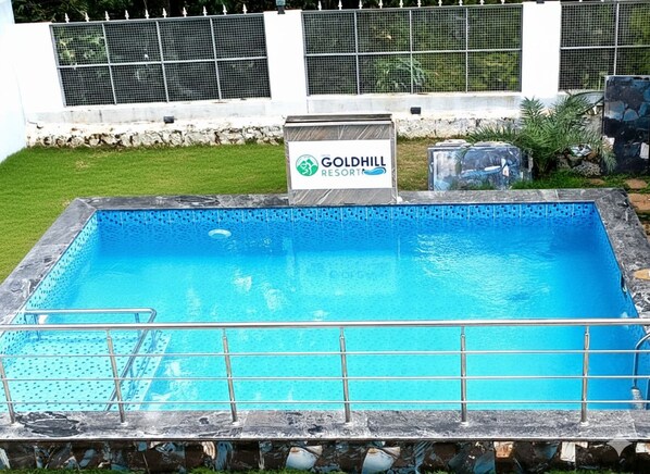 A rectangular swimming pool with a metal safety railing, surrounded by a stone border. A sign in the background reads "Goldhill Resort." - Yelagiri Gold Hill Resort (Tirupattur)