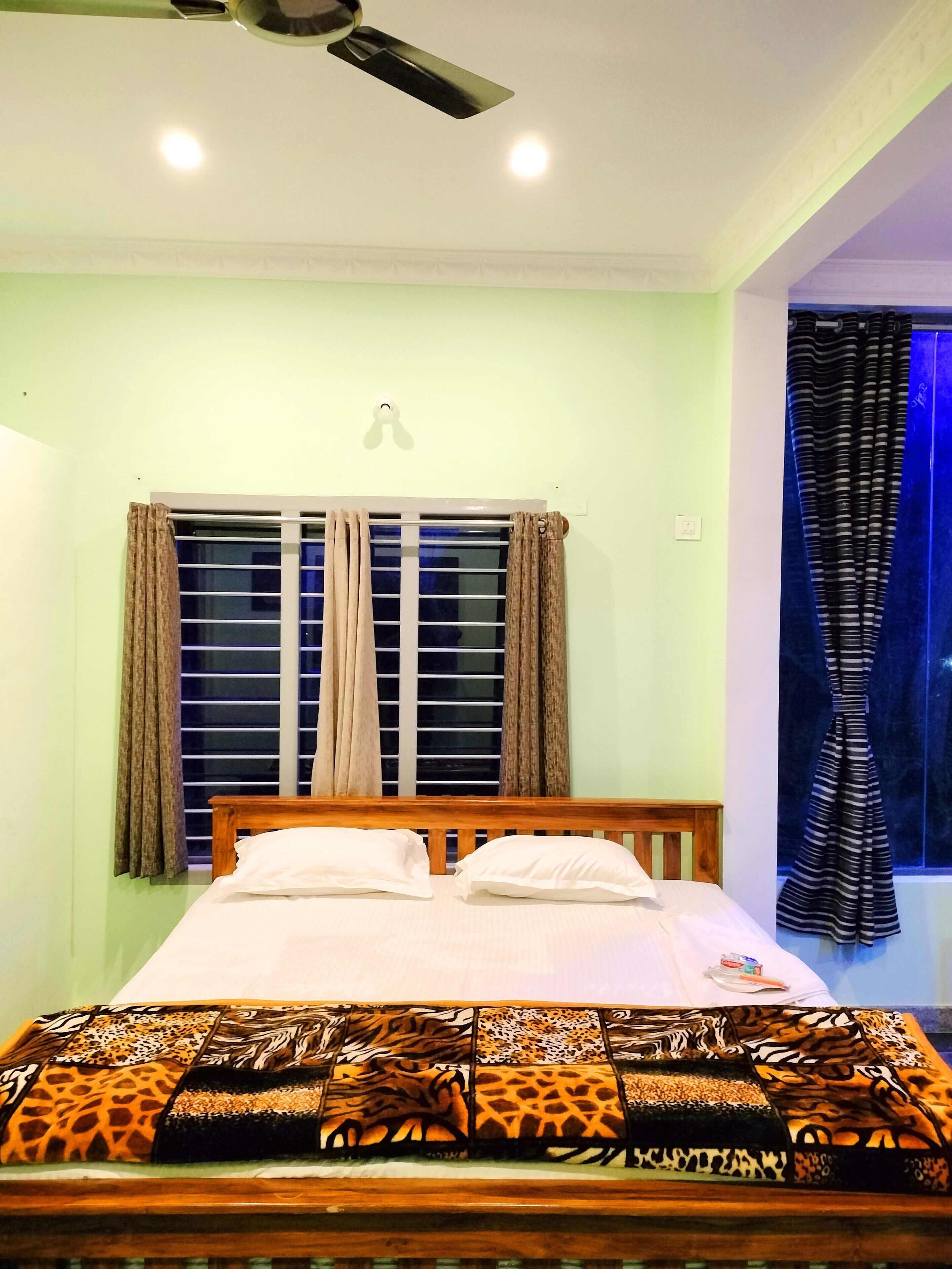 A bedroom with a bed, a window with curtains, a ceiling fan, and a view of the outside.