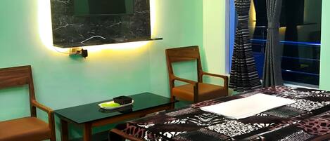 A room with a bed, a desk, two chairs, a television mounted on a wall, and a window with curtains.