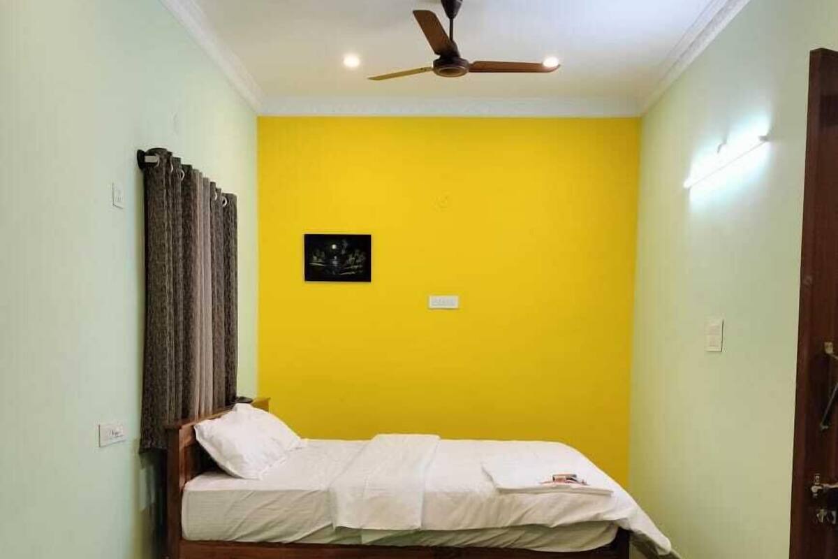 Ein Zimmer mit einem Bett, einem Deckenventilator, einer gelben Wand und einem Marmorboden.