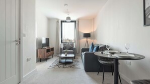 A modern living room with a sofa, a coffee table, a dining table with chairs, a TV, and a window with curtains. - Modern & Cosy 1 Bedroom Apartment in York (York)