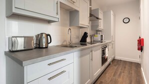 A modern kitchen with white cabinets, stainless steel appliances, and a wooden floor. - Modern & Cosy 1 Bedroom Apartment in York (York)