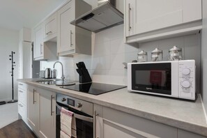 A modern kitchen with white cabinetry, a built-in oven, a microwave, and a kettle.