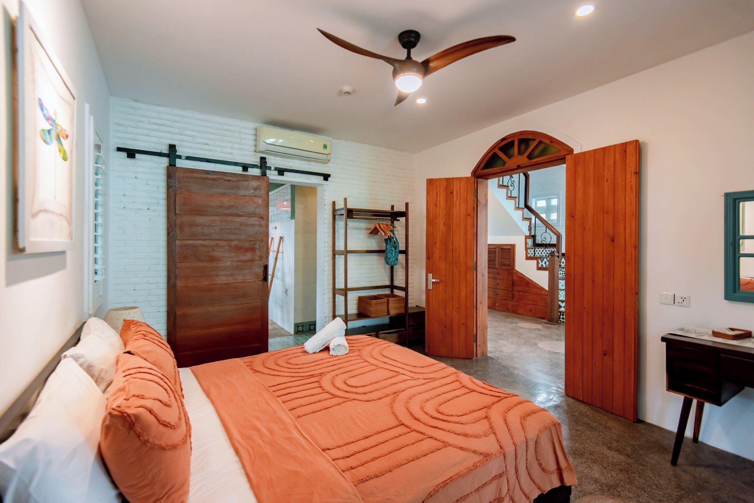 A bedroom with a bed, a ceiling fan, a wooden door, and a staircase leading to another room.