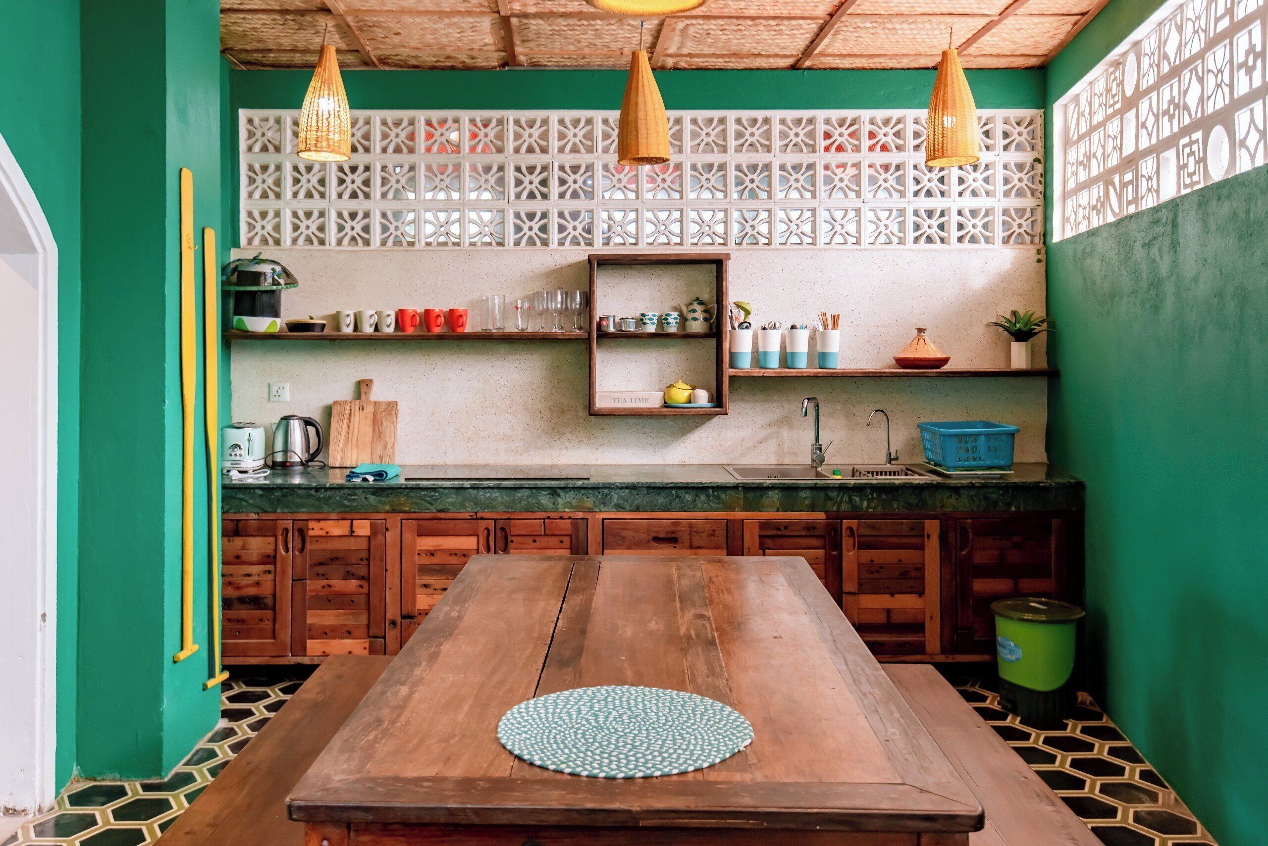Una cocina con mesa de madera, paredes verdes y piso estampado.