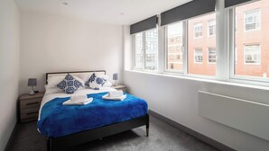 Habitación de hotel moderna con una cama grande, una mesita de noche, una lámpara y vistas a un edificio de ladrillo a través de la ventana.