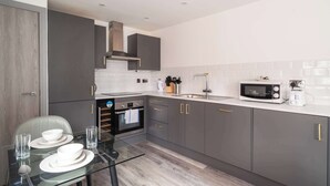Una cocina moderna con armarios grises, microondas, fregadero y una mesa de comedor de cristal dispuesta con platos y cubiertos.