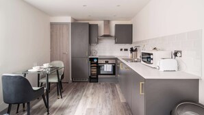 Cocina compacta con zona de comedor, que incluye microondas, tostadora, horno y un reloj en la pared.