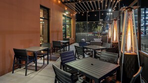 Un espacio al aire libre con mesas y sillas, luces colgantes y un calefactor grande e iluminado.