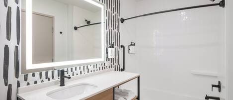 A modern bathroom with a white sink, mirror, and shower.