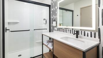 Une salle de bain moderne avec une douche à parois de verre, un lavabo blanc avec un meuble-vasque en bois et un grand miroir.