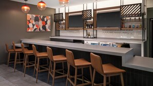 A modern kitchen with a bar area, featuring a long countertop, bar stools, pendant lighting, and a wine rack. - Atwell Suites Henderson by IHG (Henderson)
