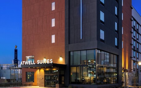 A modern hotel building with a prominent ATWELL SUITES sign, large windows, and a well-lit entrance.