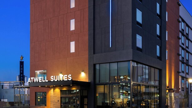 Un moderno edificio de hotel con un llamativo letrero de ATWELL SUITES, amplias ventanas y una entrada bien iluminada.