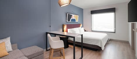 A modern bedroom with a bed, a desk, a chair, a hanging light fixture, and a window.
