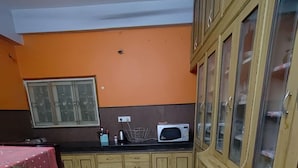 A kitchen with wooden cabinets, a microwave, and a window with a metal grill. - Hyderabad Serenity Retreat - 3 Bdrm Apartment (Hyderabad)