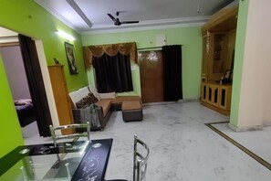A living room with a sofa, a glass dining table, and a ceiling fan. - Hyderabad Serenity Retreat - 3 Bdrm Apartment (Hyderabad)