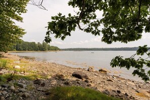 A lakeside view with rocky shore, trees, and calm water. - Tide's Rest-Oceanfront sleeps 6! (Blue Hill)