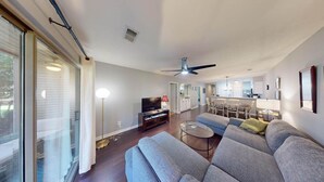 A modern living room with a sofa, TV, and a dining area in the background. - True Blue Golf Getaway 2 Bedroom (Pawleys Island)